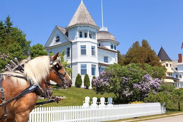Kutschpferd vor einem viktorianischen Holzhaus mit Turm und weißem Gartenzaun auf Mackinac Island