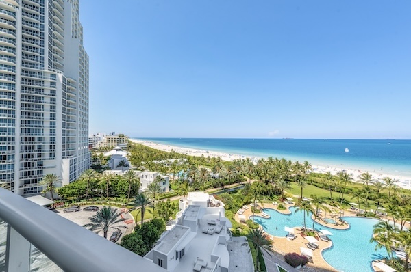 Blick von oben über Poolanlage und Palmen auf den langen Strand von Miami Beach