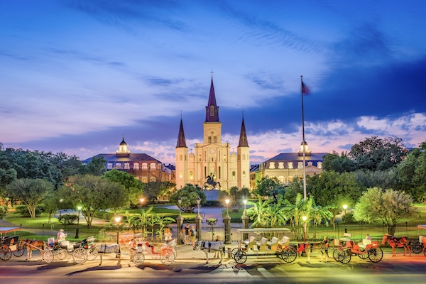 Beleuchtete Kathedrale und wartende Pferdekutschen am Jackson Square in New Orleans in der Abenddämmerung