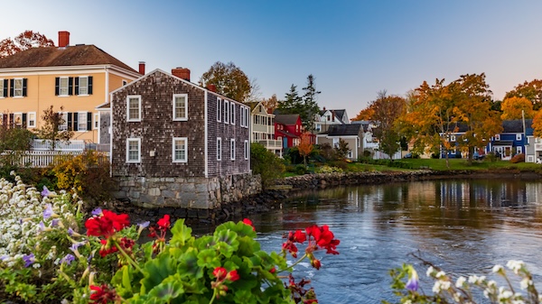 Historische Holzhäuser am Wasser in Portsmouth, im Vordergrund rote Blüten und Herbstlaub