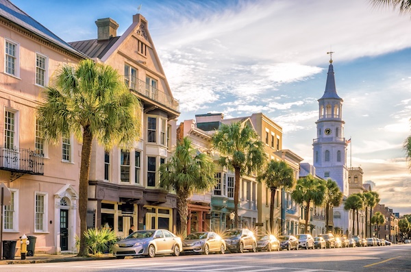 Straße mit pastellfarbenen Altstadthäusern, Palmen und weißem Kirchturm in Charleston