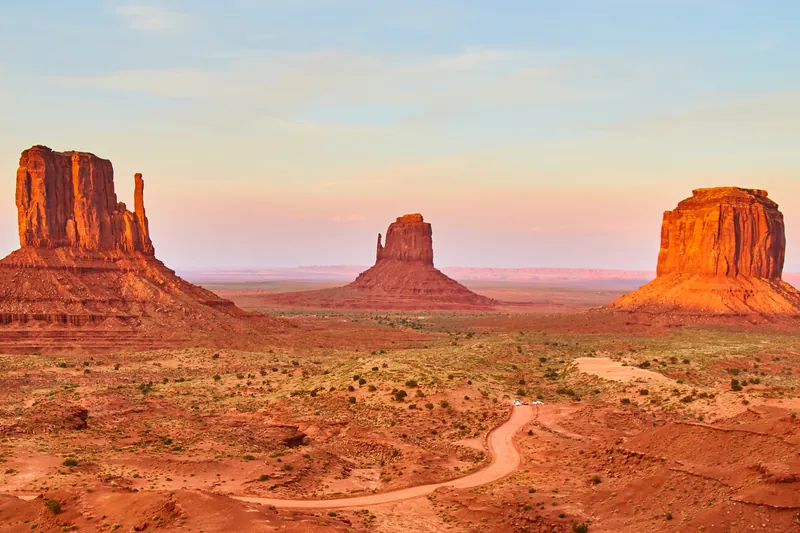 Monument Valley: drei markante Felsformationen im Abendlicht, davor die Straße durch die rote Wüste