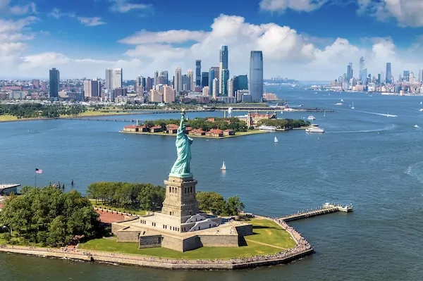 Freiheitsstatue in New York mit Blick auf die Skylnie mit blauem Himmel und Booten auf dem Wasser